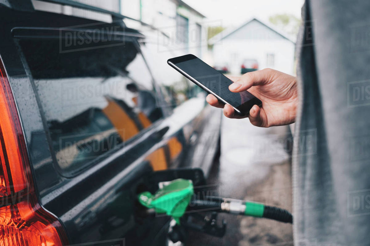 Man using mobile phone while refueling car at gas station Stock Photo
