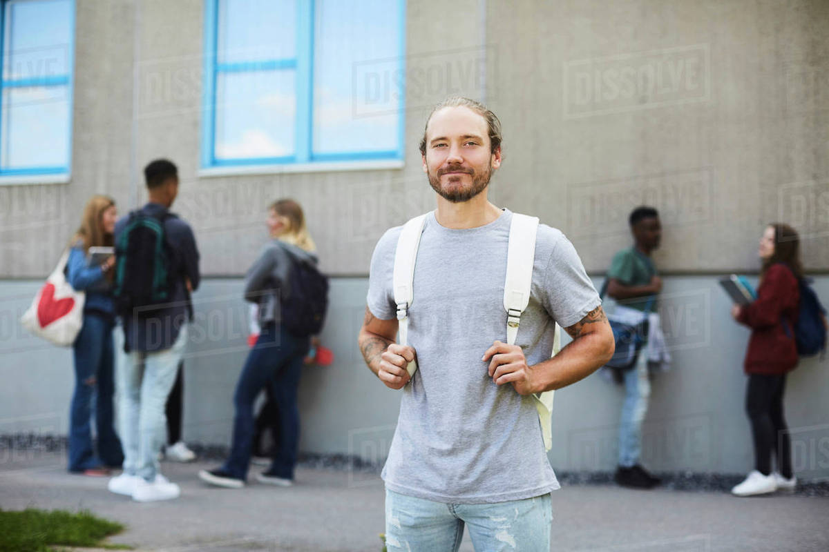 Portrait of smiling student carrying backpack standing at university