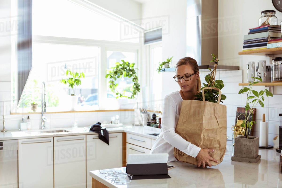 Woman Holding Paper Bag While Looking At Digital Tablet In Kitchen