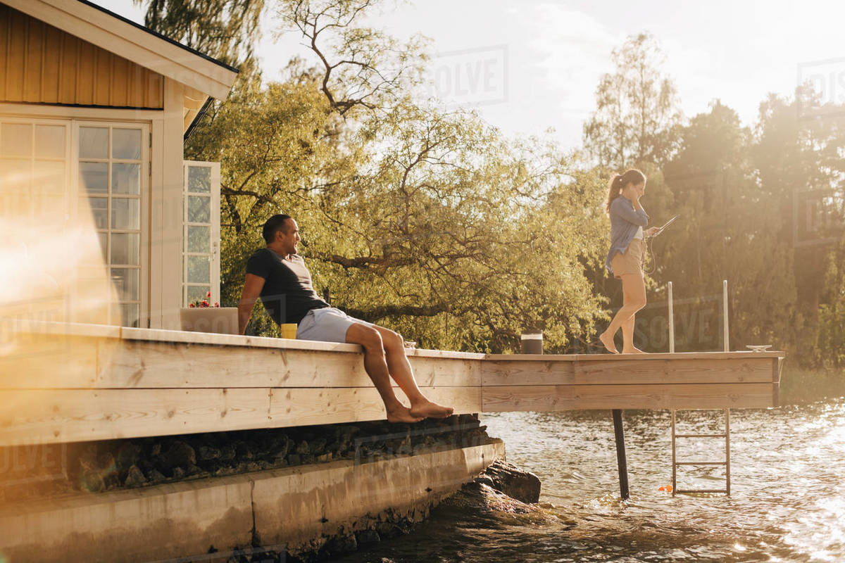 Mature man looking at woman using digital tablet while sitting on patio by lake Royalty-free stock photo