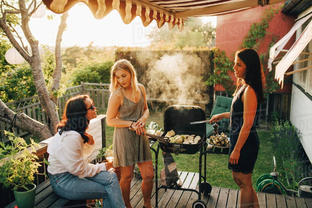 Friends talking while grilling food on barbecue for dinner party in