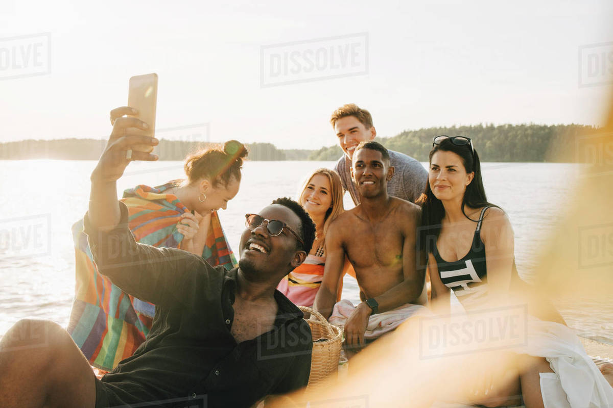 Man taking selfie with happy friends through smart phone on jetty in summer Royalty-free stock photo