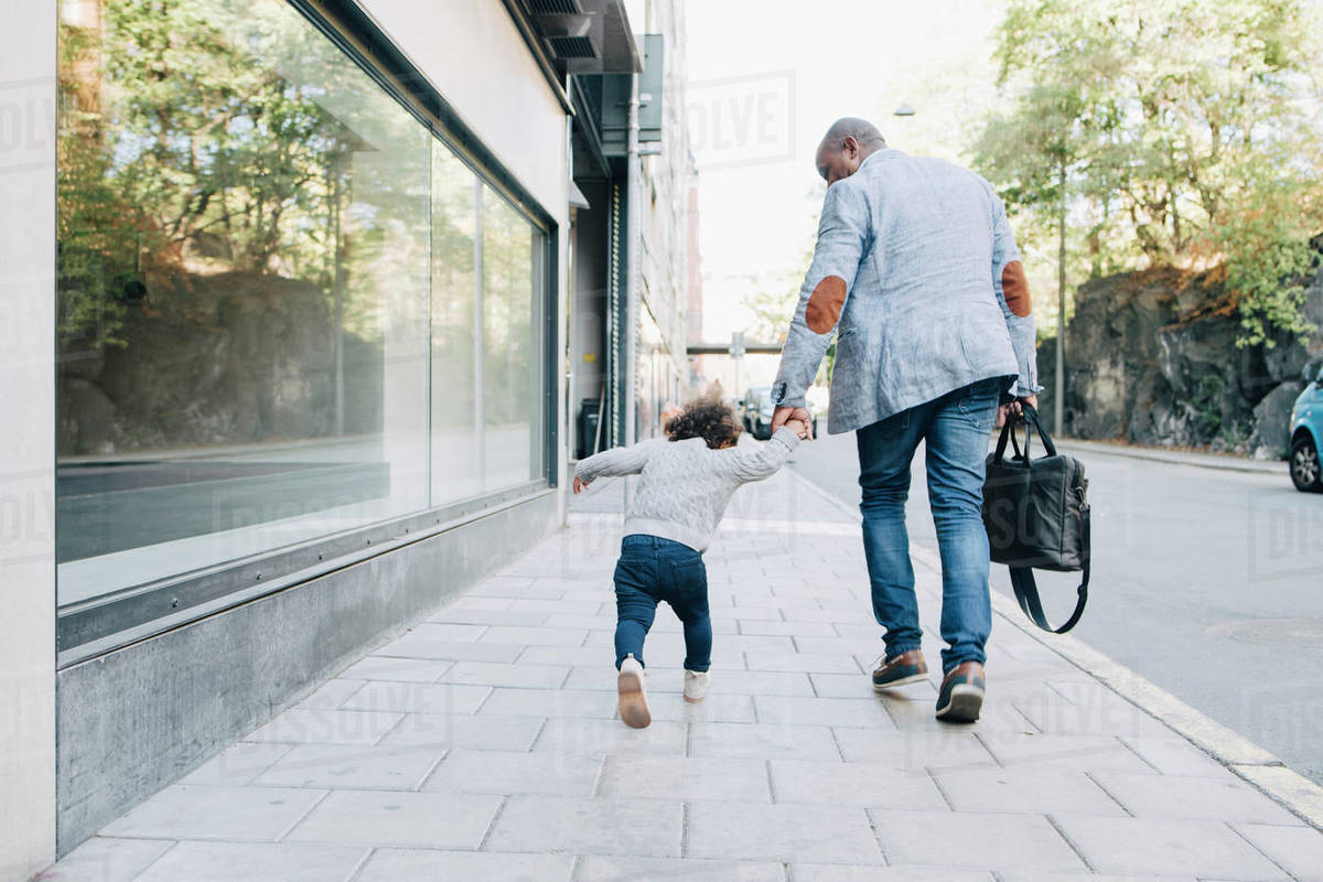 Rear view of father and daughter walking on sidewalk in city Royalty-free stock photo