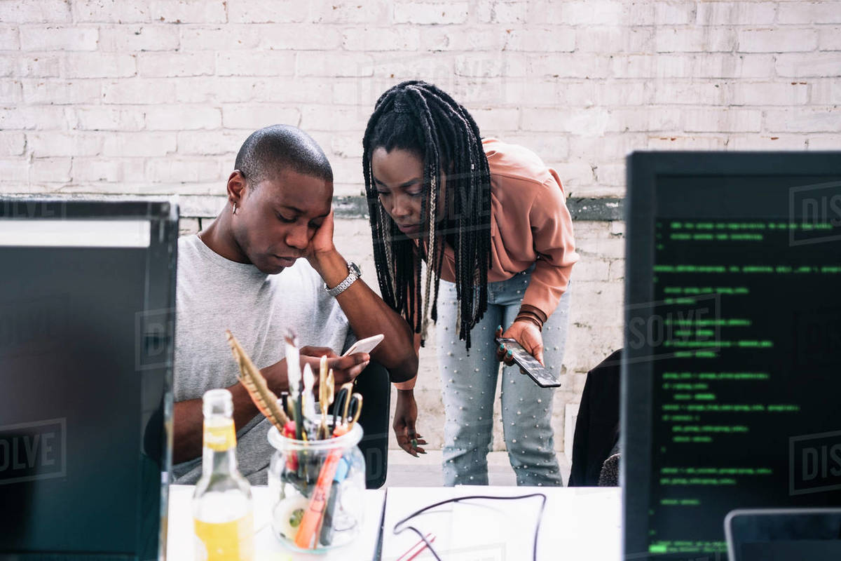 Young businesswoman looking at businessman using smart phone in creative office Royalty-free stock photo