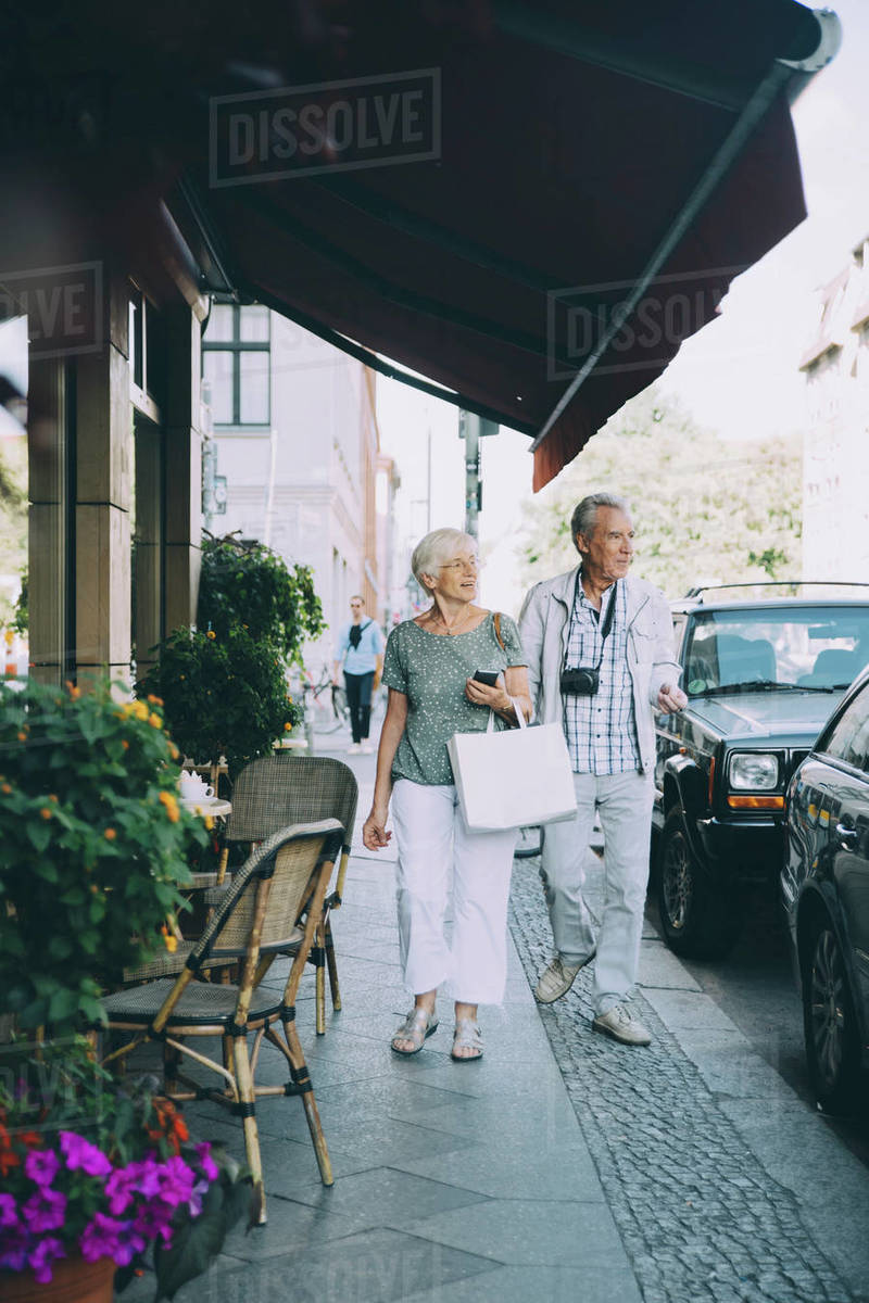 Full length of elderly couple walking on sidewalk in city Stock Photo