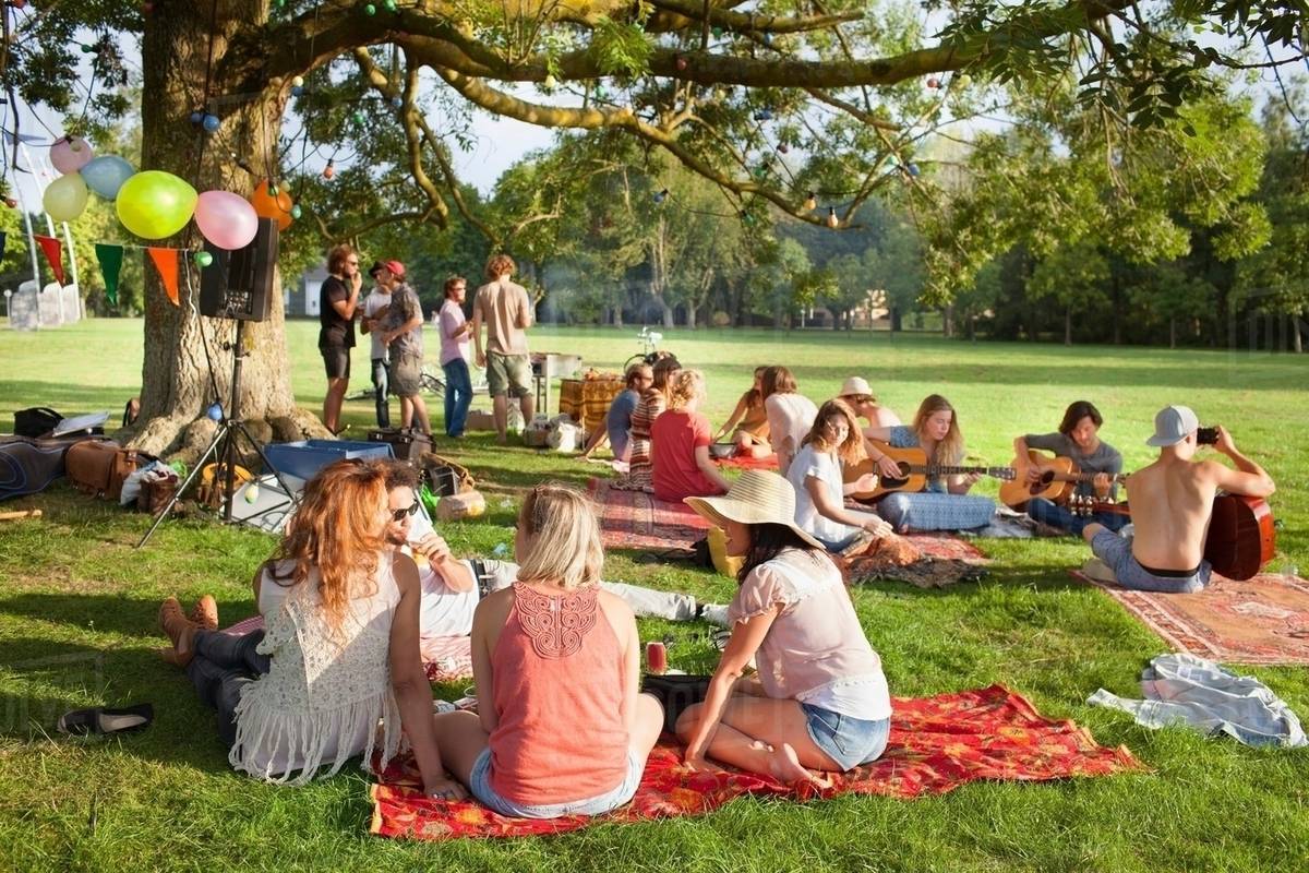Group of friends listening to music under park tree at sunset party