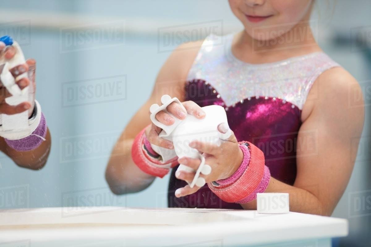 Young gymnasts applying chalk powder to hands before using bars, mid