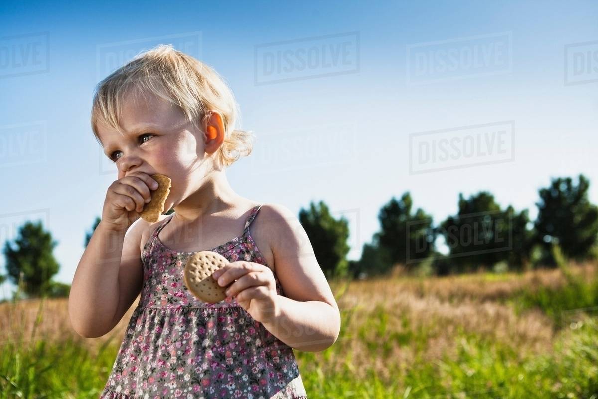 Toddler girl eating crackers outdoors Stock Photo Dissolve