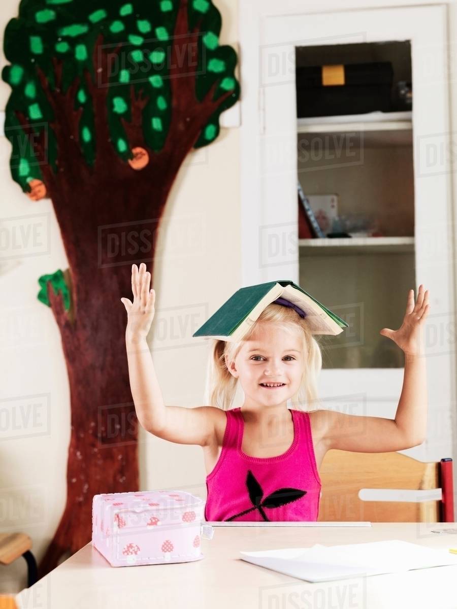Girl balancing book on head at desk Stock Photo Dissolve