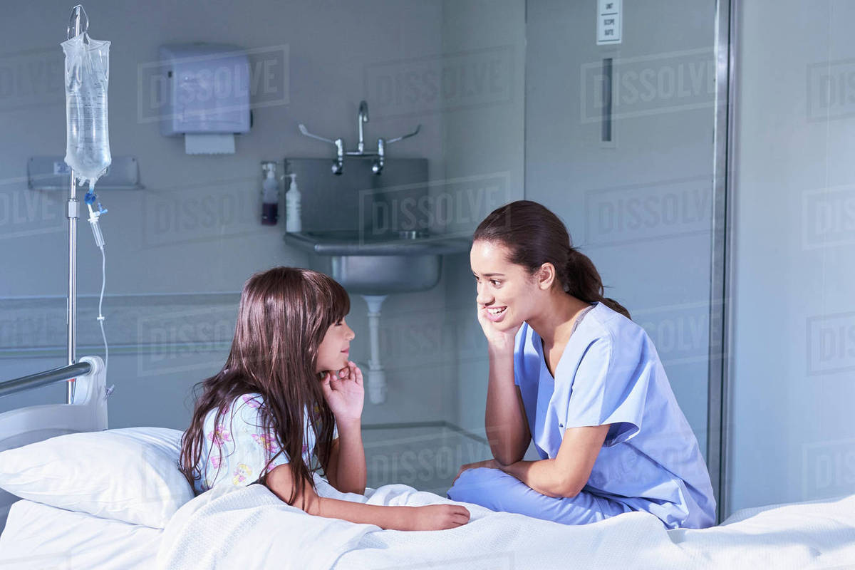 Nurse talking with girl patient sitting up in bed on hospital children's ward Stock Photo