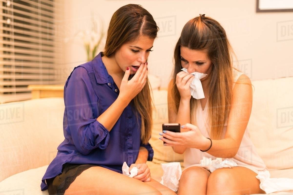 Two young women, sitting on sofa looking at smartphone, shocked