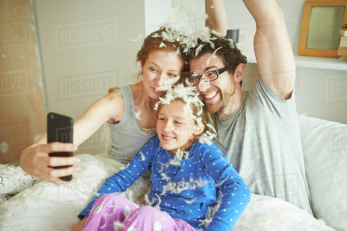 Mid Adult Couple And Daughter Covered In Pillow Fight Feathers