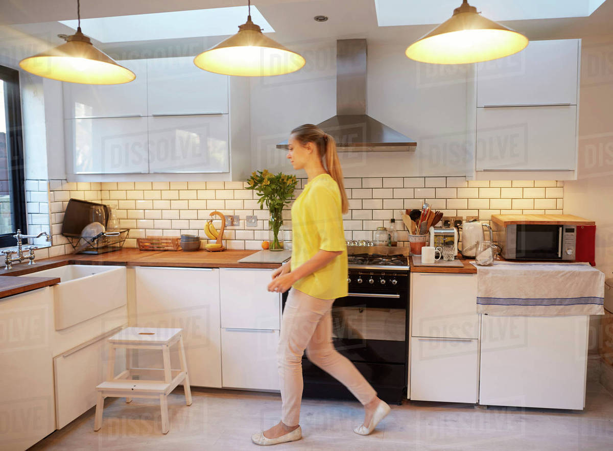 Mid adult woman walking in stylish kitchen Stock Photo Dissolve