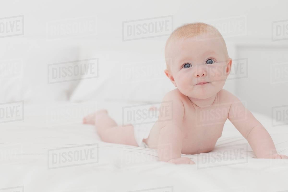 Smiling baby laying on bed Stock Photo Dissolve
