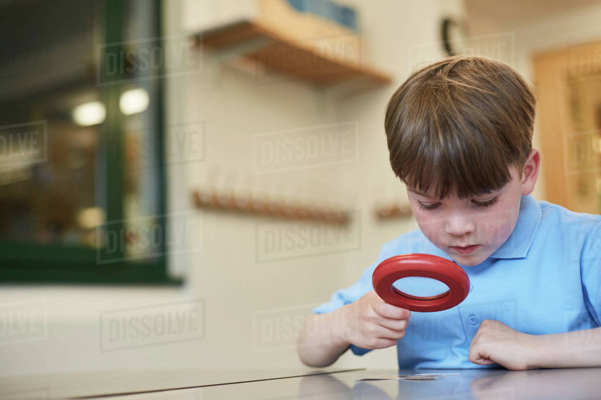 Schoolboy looking through magnifying glass in classroom lesson at primary school Stock Photo