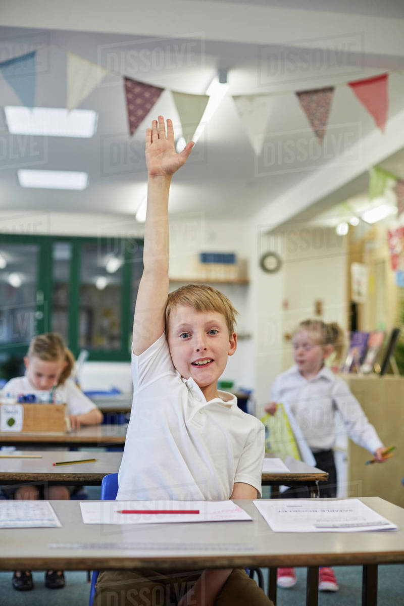 Schoolboy with hand up in classroom at primary school Stock Photo