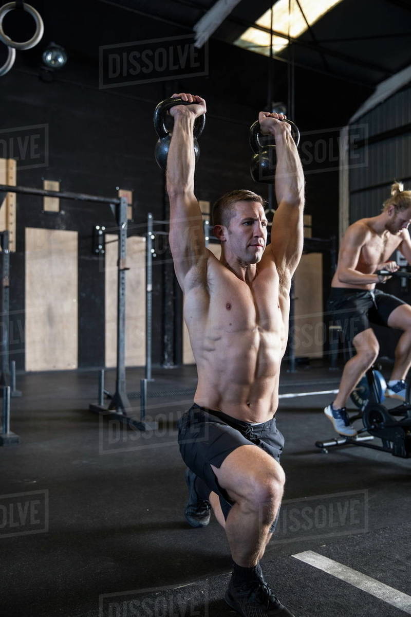 Two men exercising in gymnasium, using kettlebells and air resistance exercise bike Stock