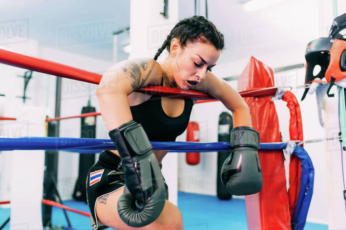 Exhausted female boxer leaning over boxing ring ropes Stock Photo