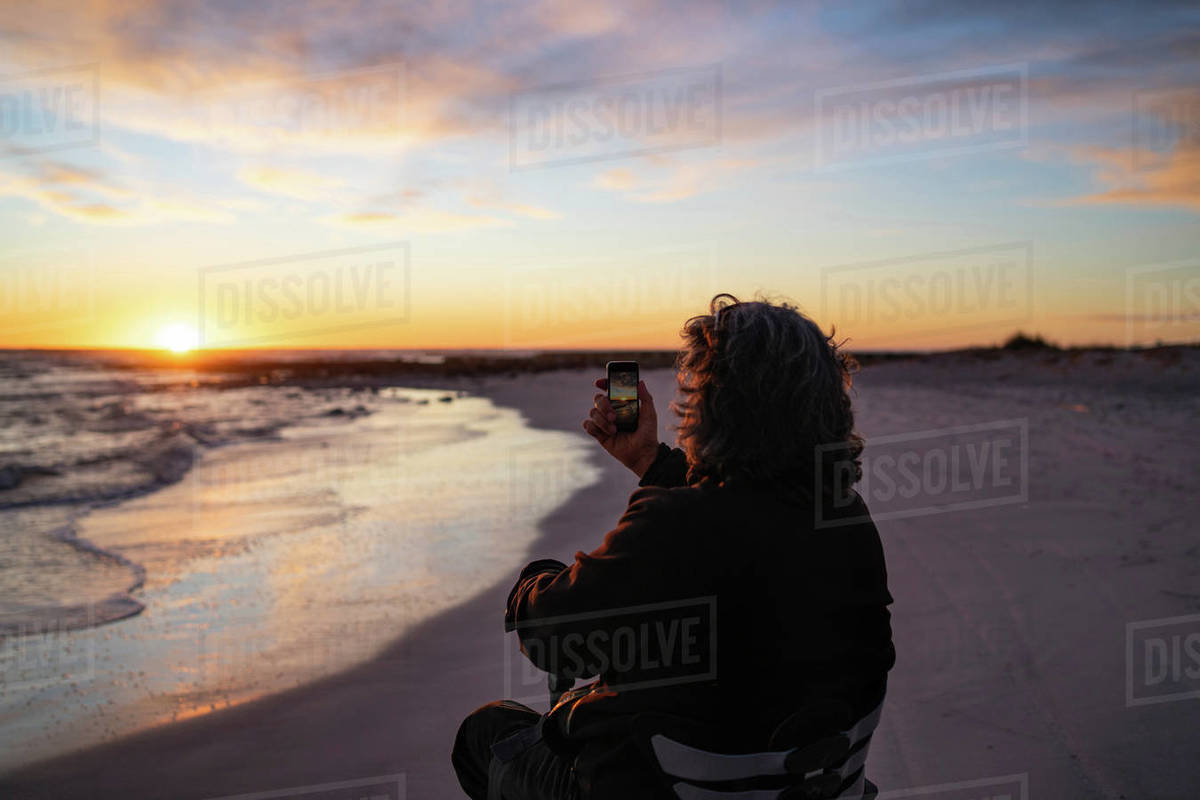 Man on wheels taking photograph of sunset with smartphone at seaside Royalty-free stock photo