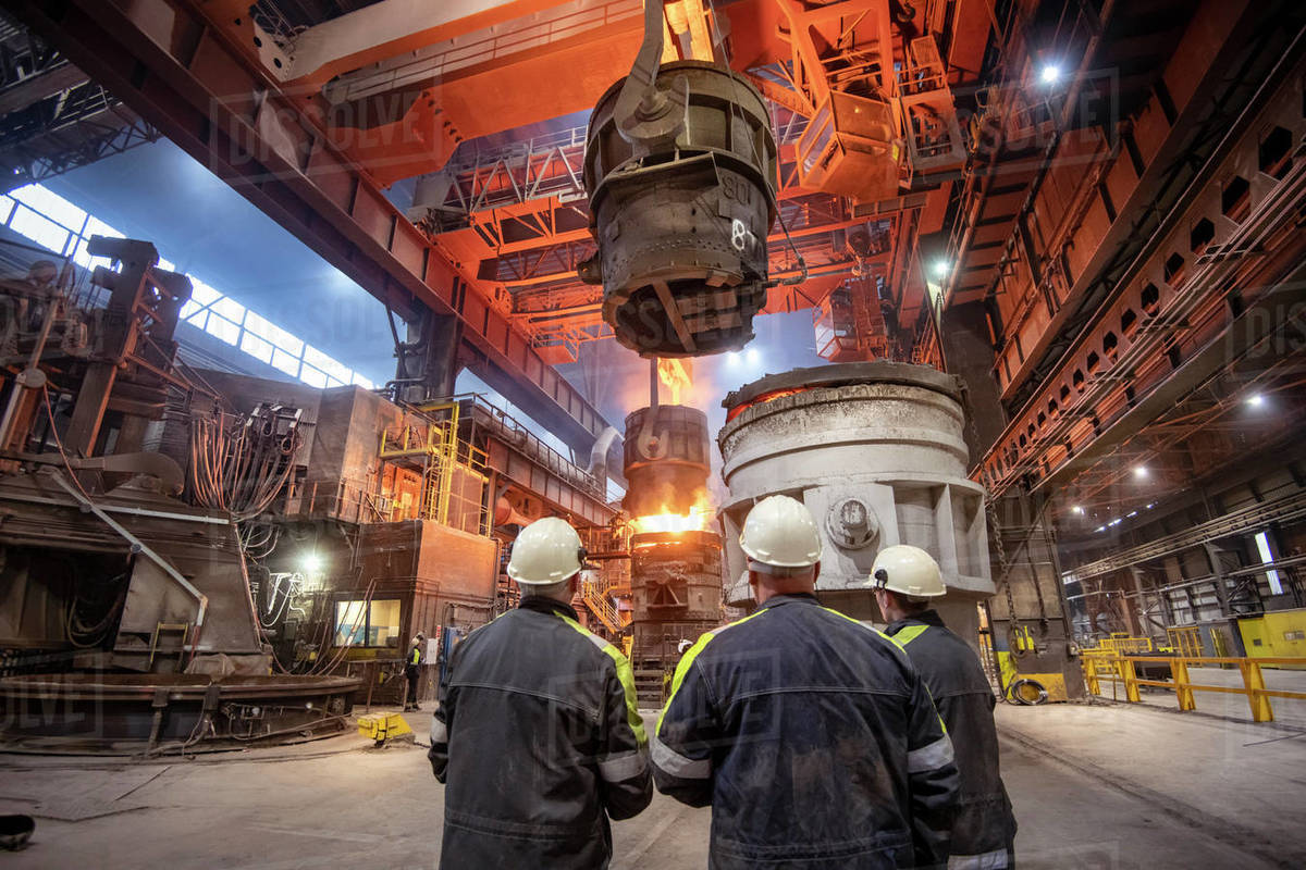 Three steelworkers watching molten steel pour in steelworks Royalty-free stock photo