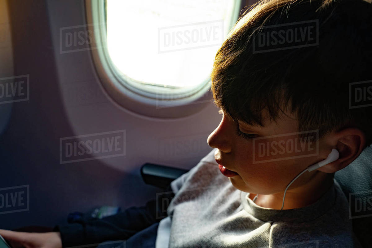 Teenage boy listening to music on earphones during airplane journey