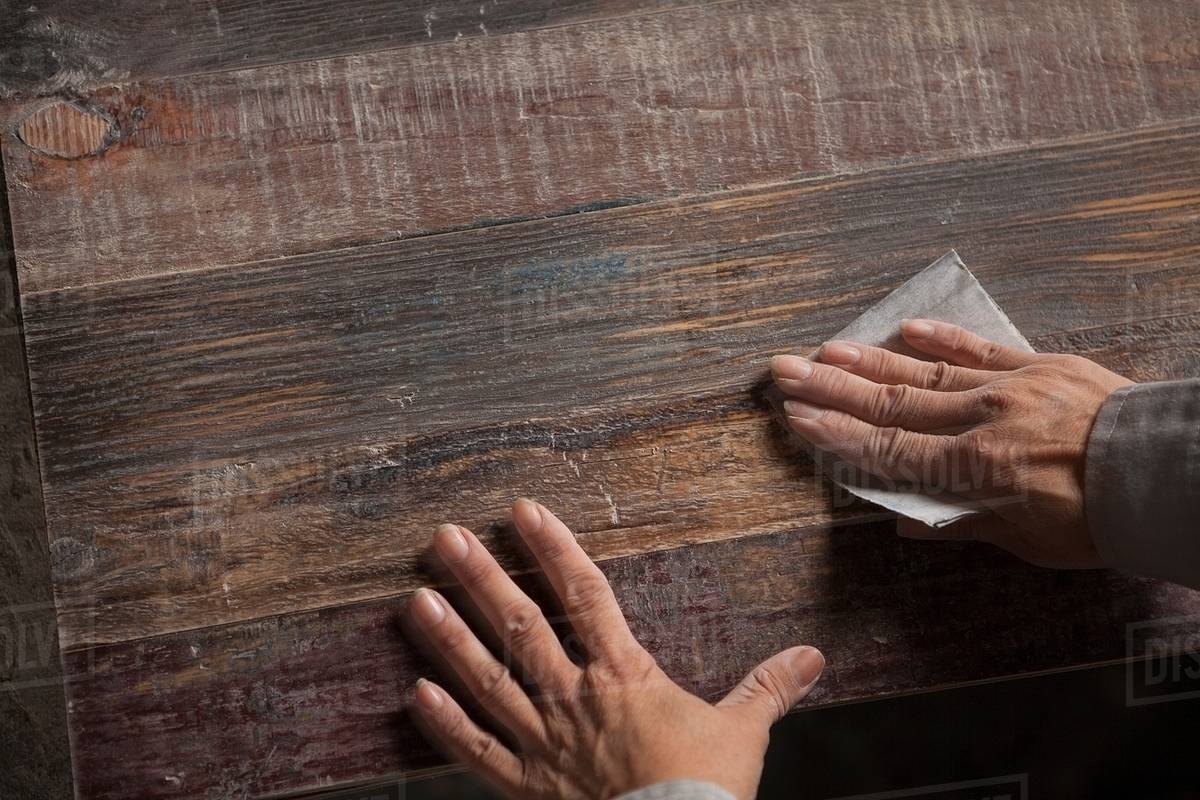 Carpenter smoothing surface of wood plank with sandpaper in factory