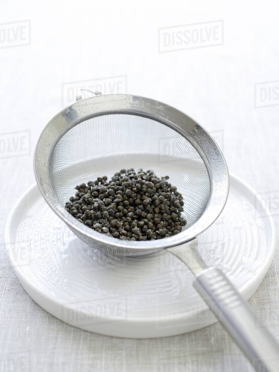 Baby capers in sieve on plate Stock Photo Dissolve