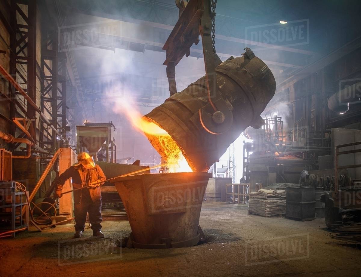 Steel worker cleaning large ladle in an industrial foundry Stock