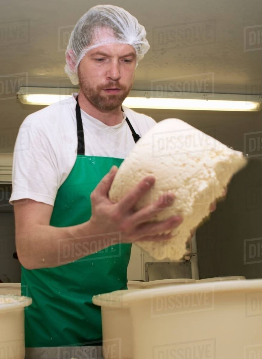 Cheesemaker holding part processed cheese round at farm factory Stock