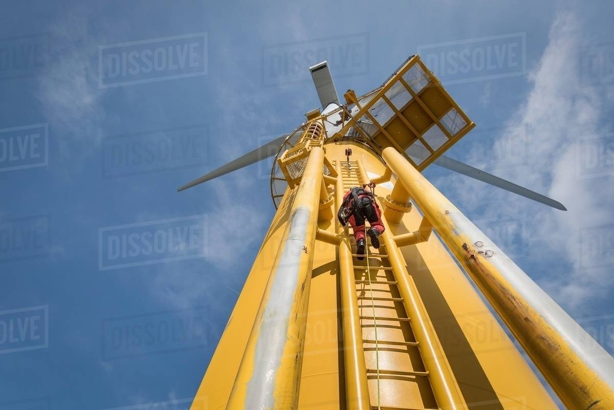 Engineer climbing ladder of wind turbine from boat at offshore windfarm