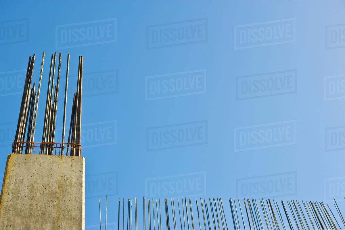 Exposed rebar protruding from unfinished concrete column against blue sky, low angle view