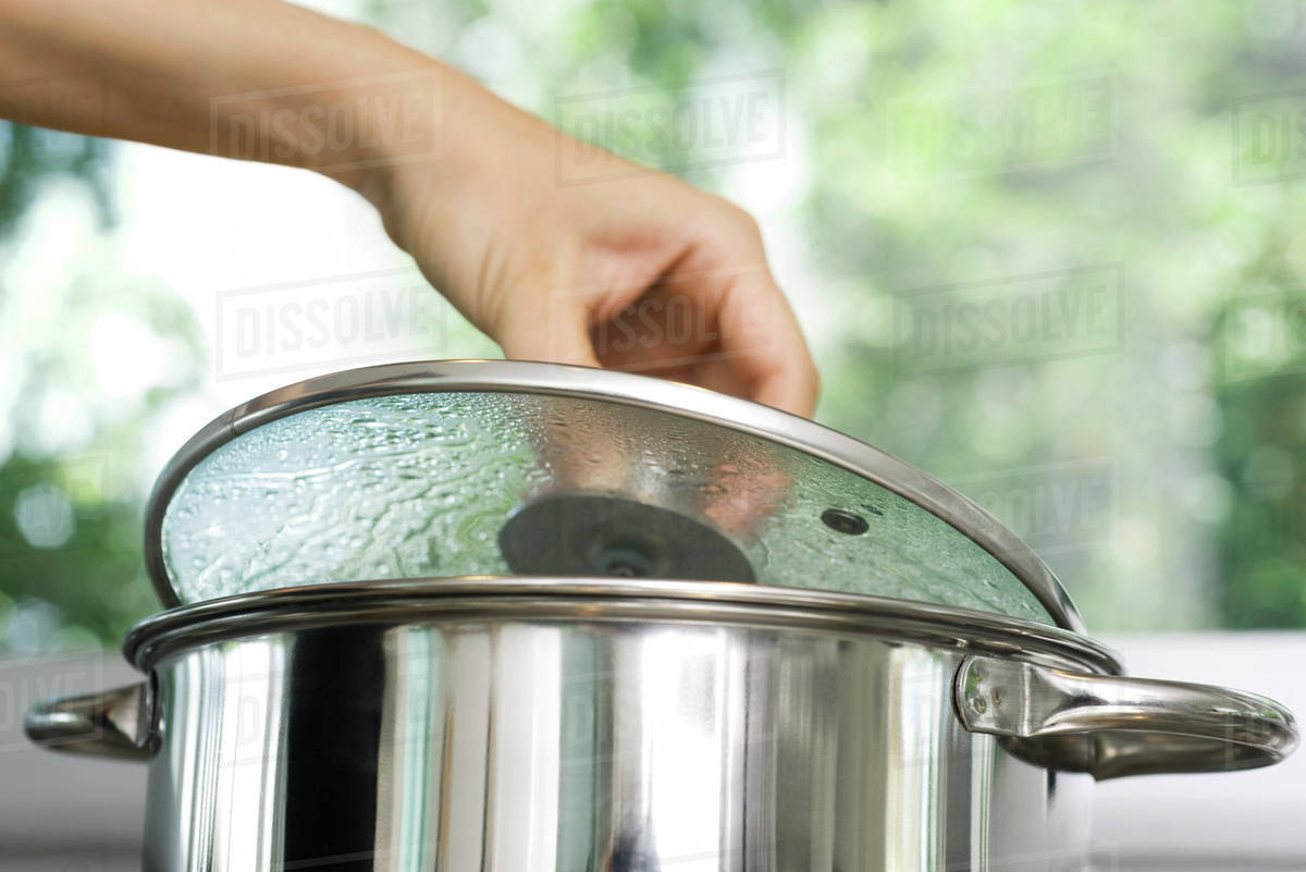 Person removing lid from cooking pot Stock Photo Dissolve