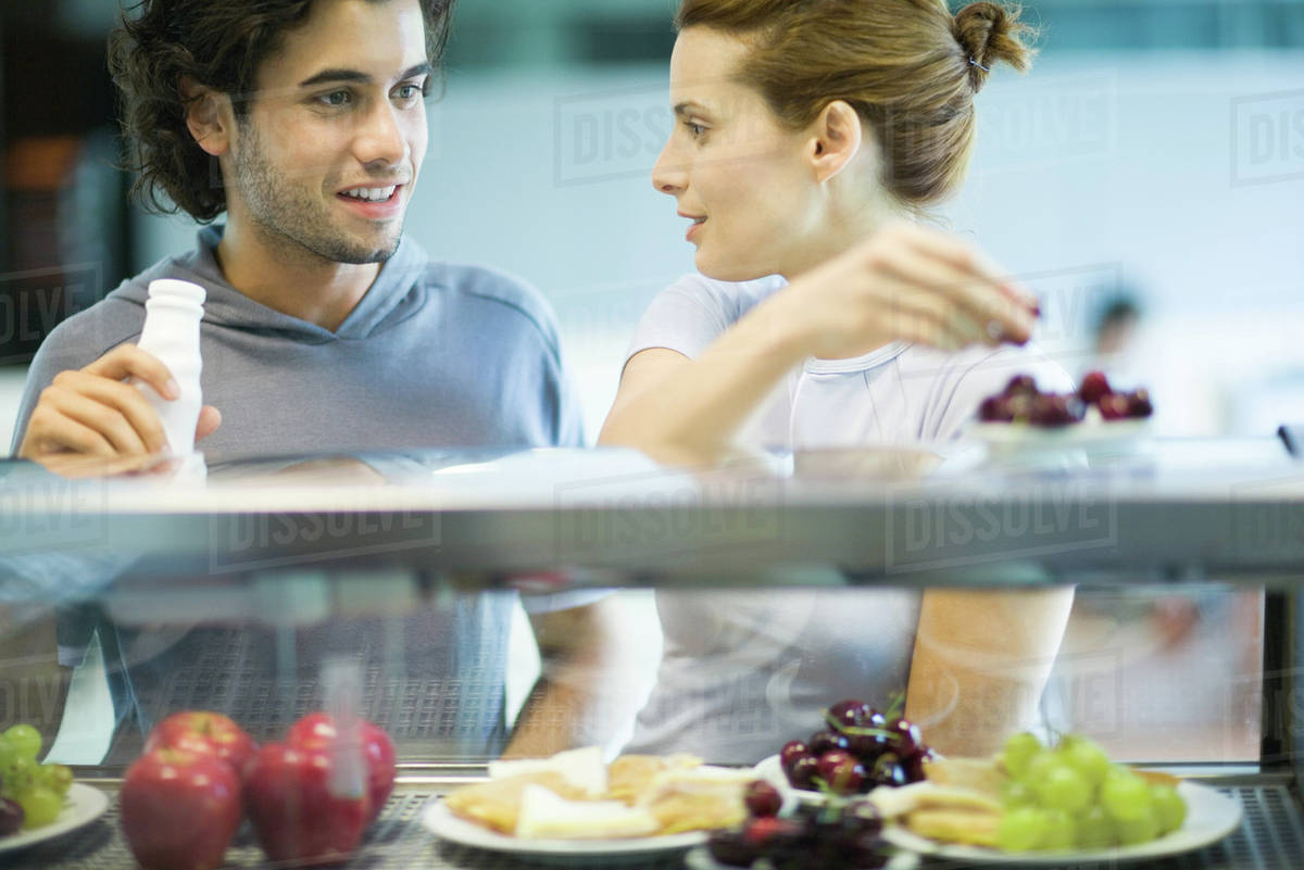 Two young adults standing at snackbar, chatting Stock Photo Dissolve