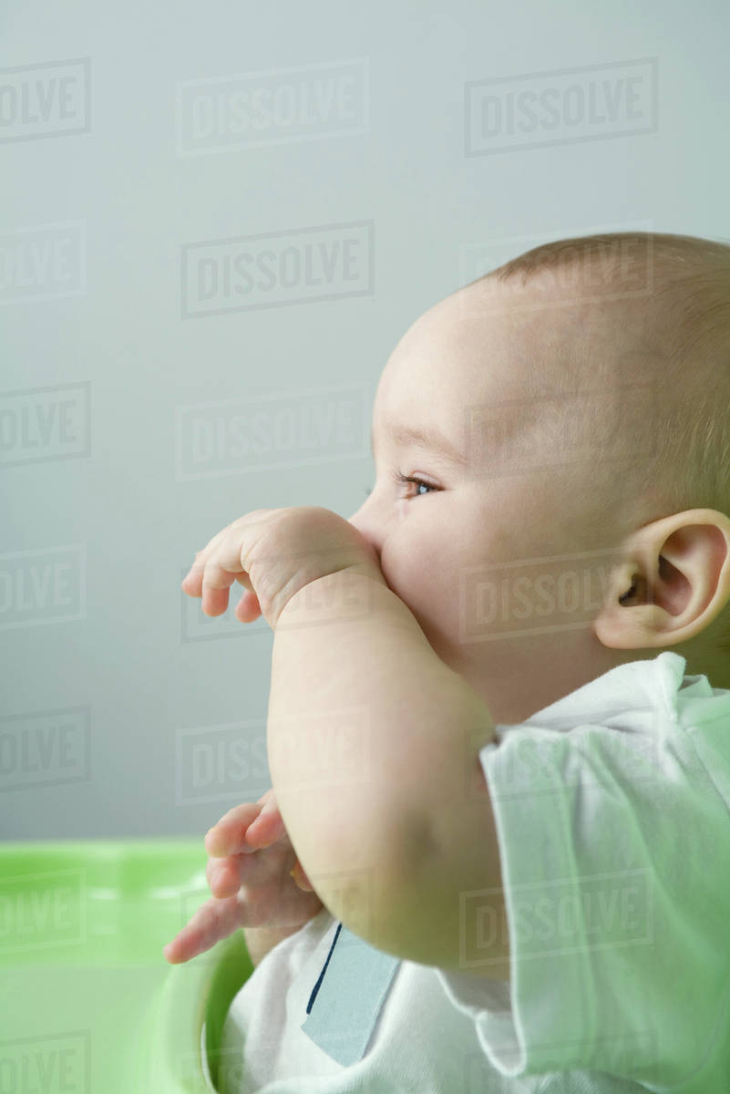 Baby sitting in high chair, wiping face Stock Photo Dissolve