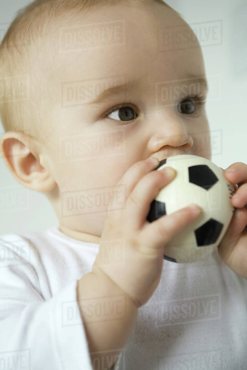 Baby putting toy soccer ball in mouth, closeup Stock Photo Dissolve