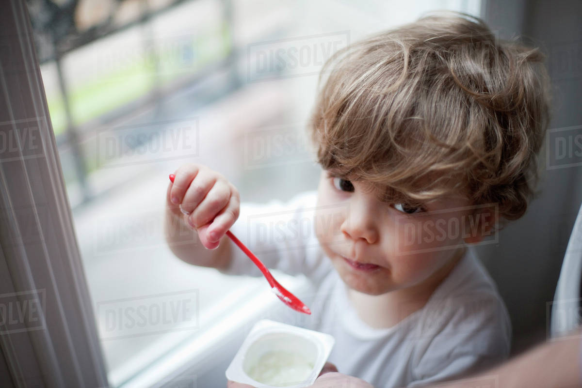 Toddler boy eating yogurt, portrait Stock Photo Dissolve