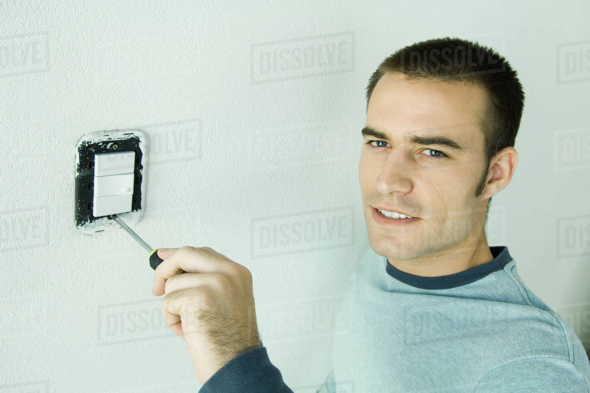 Man removing light switch cover from wall Stock Photo Dissolve