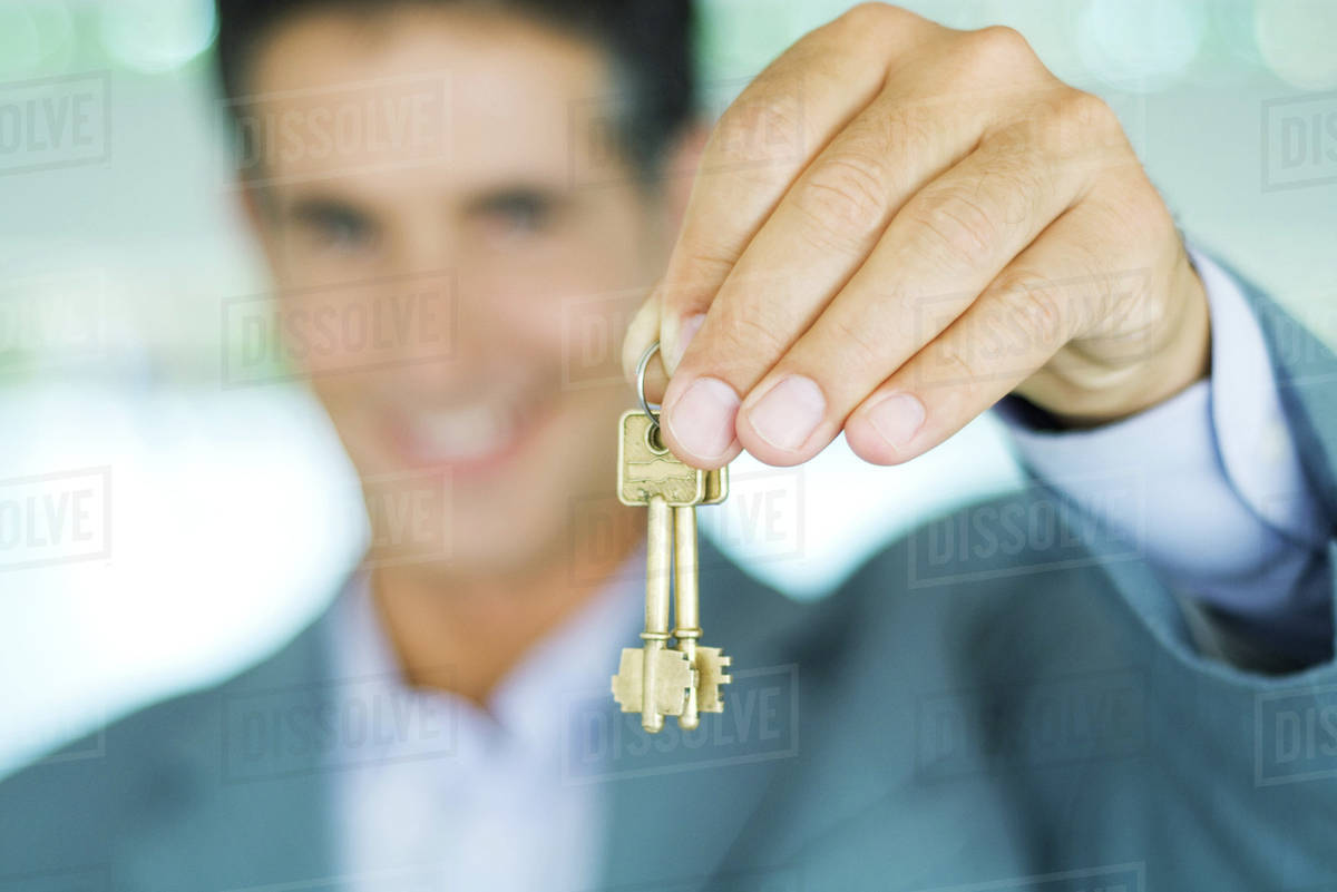 Man in suit holding up keys, focus on hand holding keys in foreground