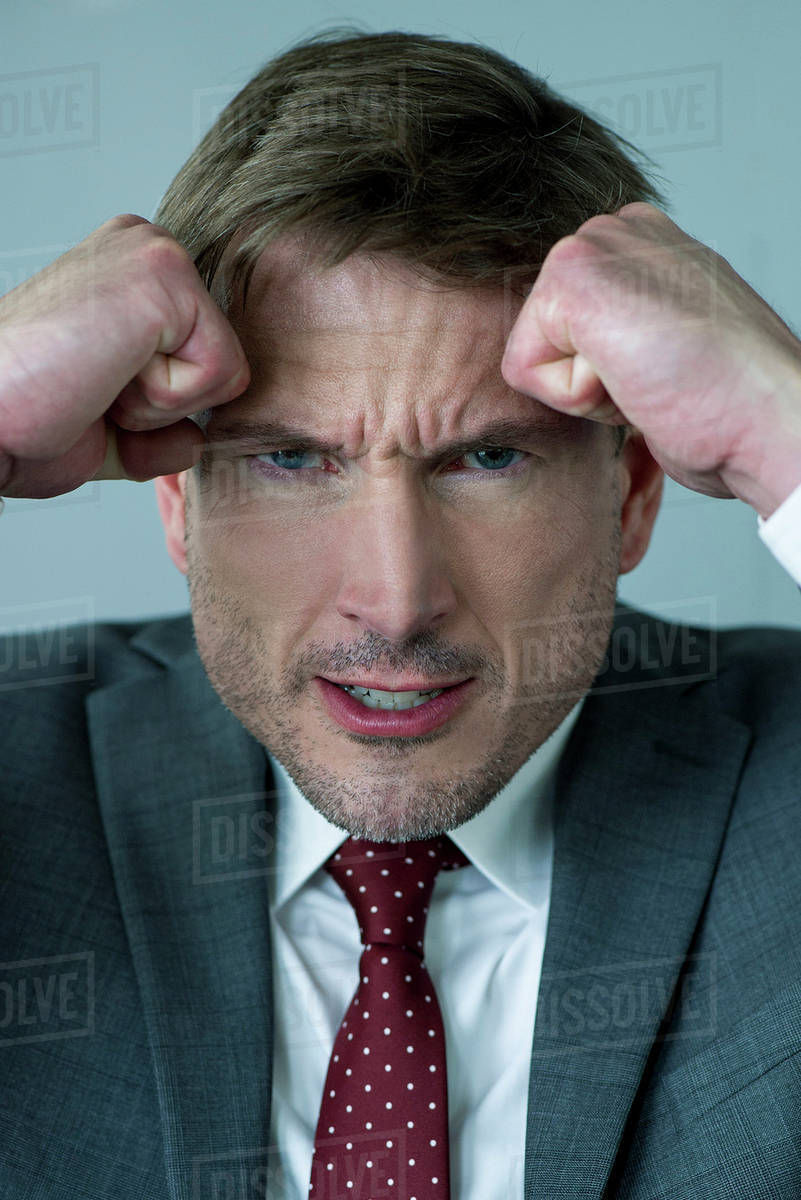 Businessman holding clenched fists against head in anger, portrait