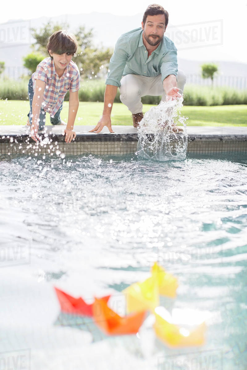 Father and son racing paper boats in swimming pool Stock Photo Dissolve