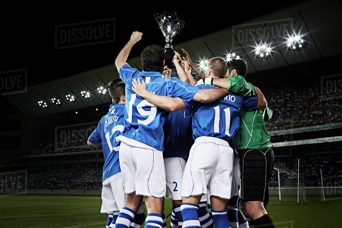 Soccer team cheering with trophy on field Stock Photo Dissolve