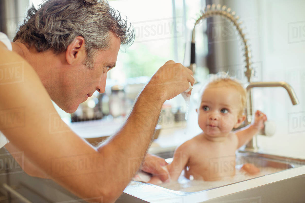 Father Bathing Baby In Kitchen Sink Stock Photo