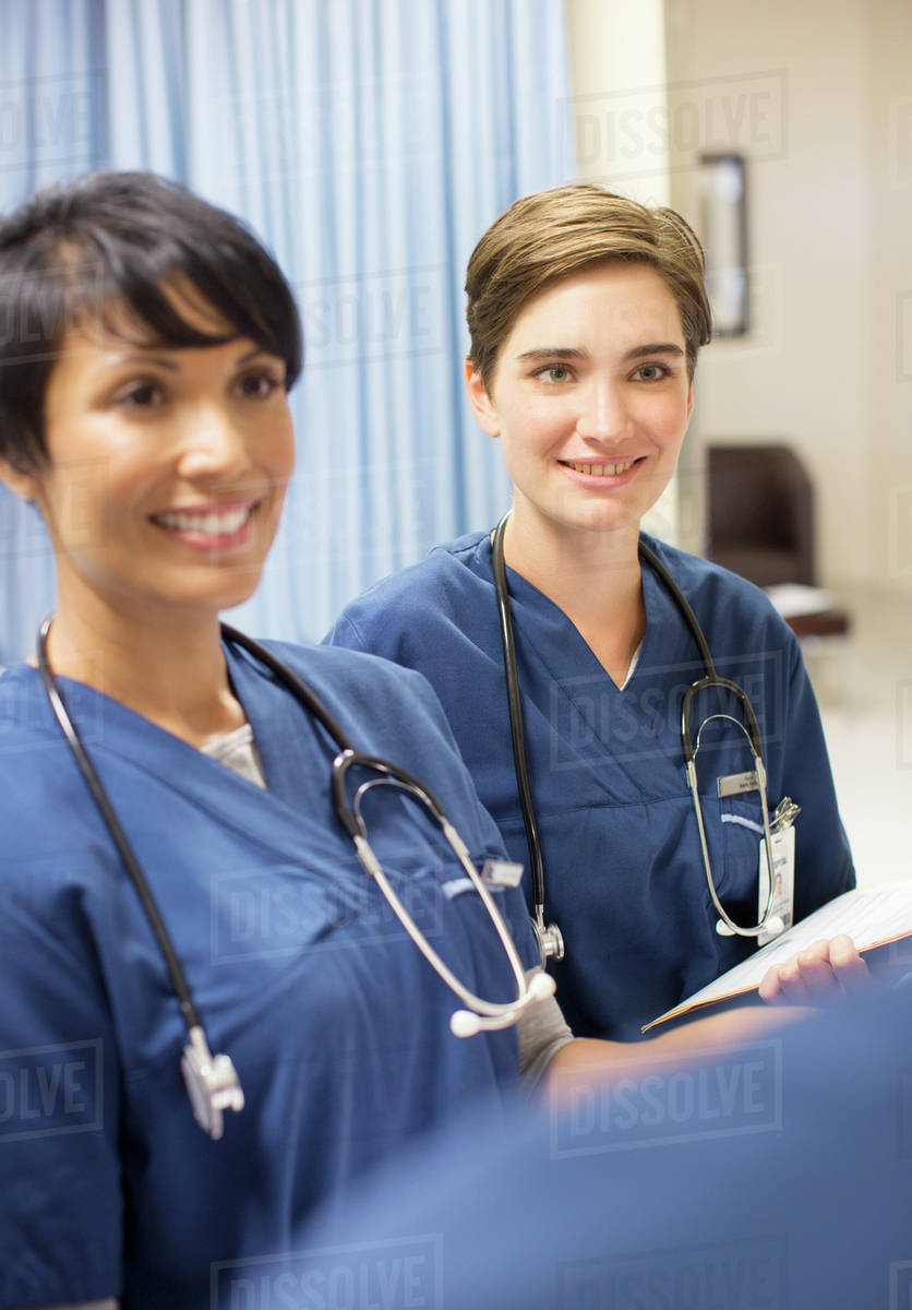 Two smiling doctors wearing scrubs with stethoscopes around necks in