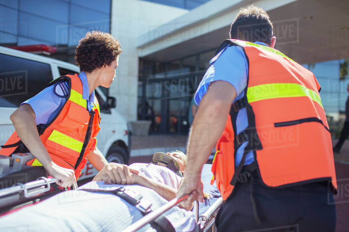 Paramedics wheeling patient in hospital parking lot Stock Photo