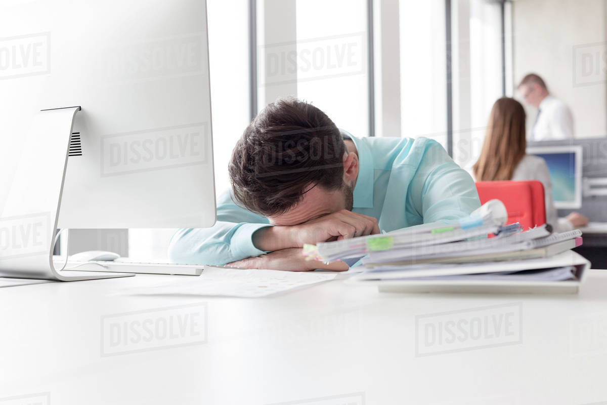 Frustrated businessman with head down next to stack of reports on desk