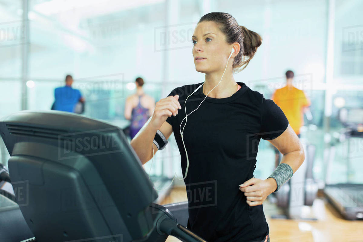 Focused woman running on treadmill with headphones at gym Stock Photo