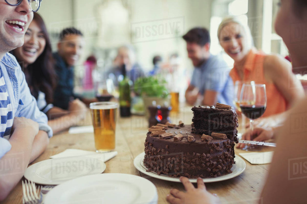 Woman serving chocolate birthday cake to friends at restaurant