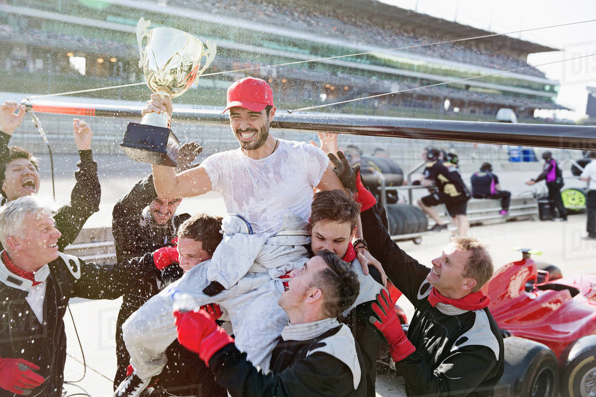 Formula one racing team carrying driver with trophy on shoulders, celebrating victory on sports track Royalty-free stock photo