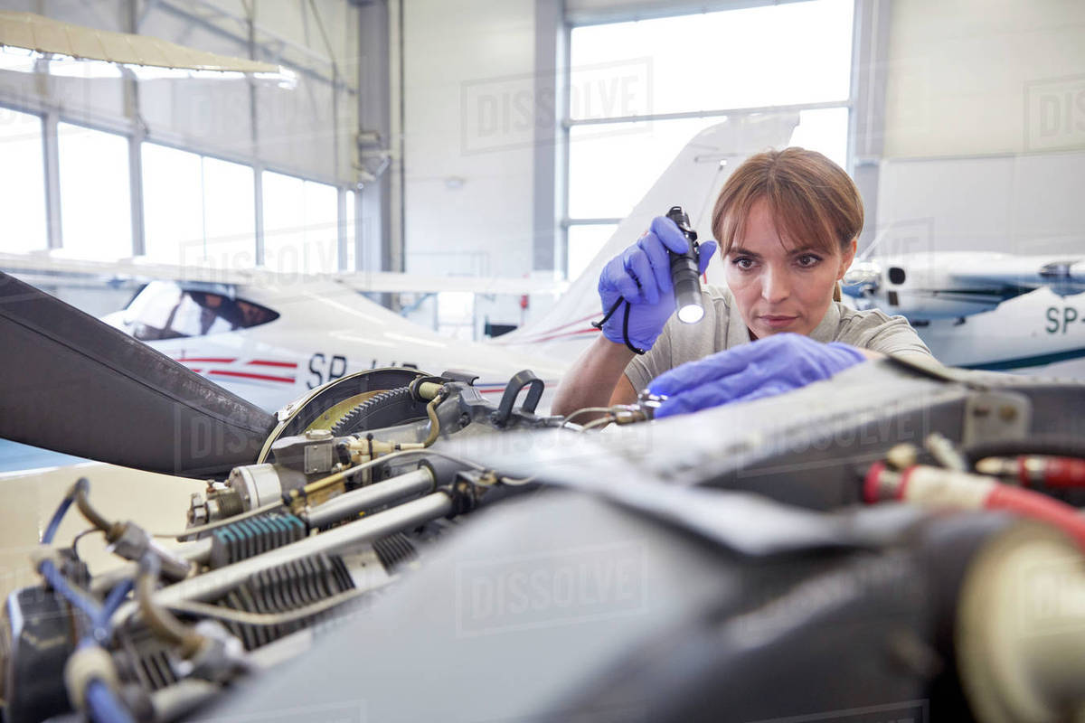 Focused female engineer mechanic with flashlight examining airplane