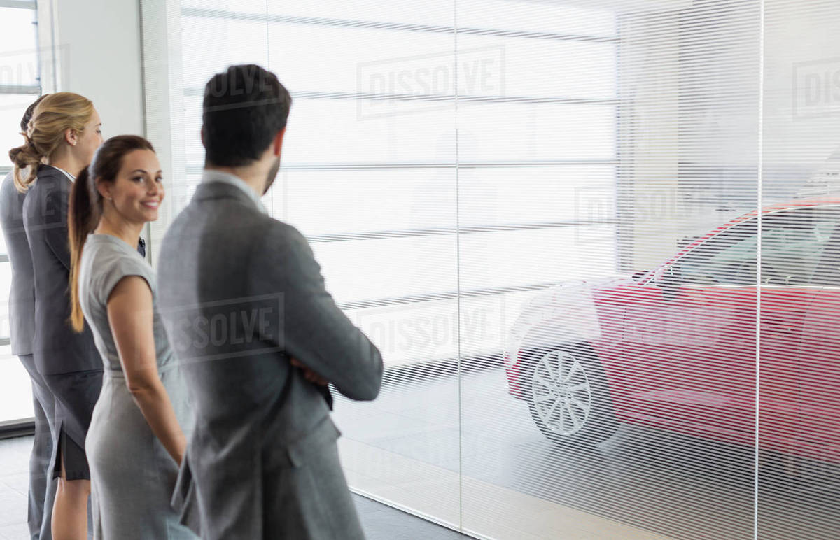 Car sales people looking at new, red car in car dealership showroom